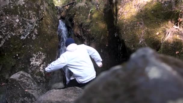 一个穿着白色夹克的人下到峡谷里的瀑布上 游客站在石头上 看着峡谷中落水的流动 — 图库视频影像