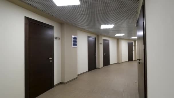 Couloir rond vide avec murs beige clair et portes fermées brun foncé. Portes fermées le long d'un couloir éclairé dans l'immeuble à bureaux . — Video