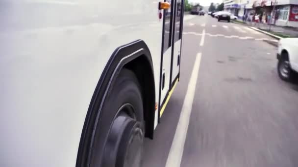 Vista de perto das rodas e pneus na estrada de um ônibus andando pela cidade, voltas no tempo. Cena. Ônibus branco desce a rua no centro da cidade . — Vídeo de Stock