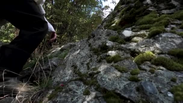 Cierre para las piernas del escalador haciendo pasos hacia un pico de una montaña. Filmación. Senderismo botas de goma y piernas trepando por sendero rocoso sobre fondo de cielo brillante . — Vídeos de Stock