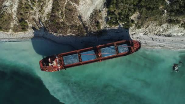 Luchtfoto bovenaanzicht van een lege, rode schip afgemeerd in de buurt van de kust van de prachtige blauwe zee. Grote industriële schip permanent in de buurt van de heuvel met groene bomen. — Stockvideo