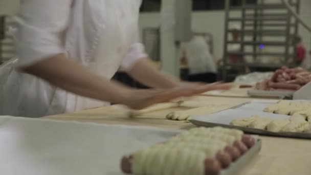 Close up for sausages wrapped in raw puff pastry at the bakery and a baker woman rolling out dough. Raw hot dogs rolled in dough by woman baker hands, food preparing concept. — Stock Video