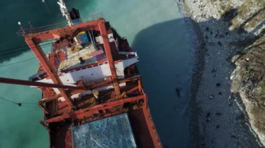 Bir boş, kırmızı habersiz hava üstten görünüm güzel mavi deniz kıyıya yakın yerde palamarla. Büyük endüstriyel gemi yeşil ağaçlar ile hill yakınındaki ayakta.