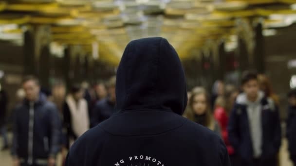Achteraanzicht van een man met een donker blauwe hoodie op staande voor een menigte op het station, weerstand concept. Close-up voor man terug voor veel mensen in de metro. — Stockvideo