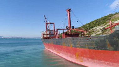 Hava deniz kıyıya yakın yerde bir yamaç boyunca demirlemiş kırmızı, boş barge için mavi gökyüzü arka plan üzerinde yeşil ağaçları ile kaplı. Bir yaz, güneşli günde büyük kargo gemisi için yakın çekim.
