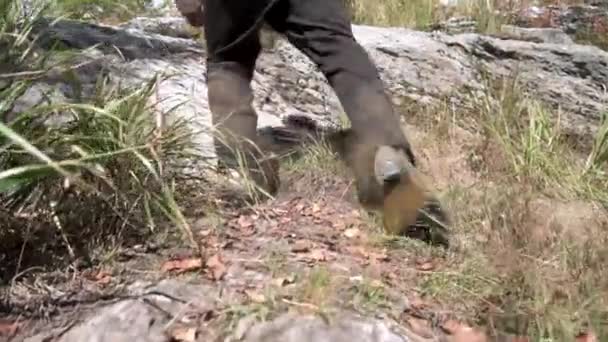 在枯草中的山上徒步时 关闭了人的橡胶靴 徒步男子的腿爬上陡峭的岩石斜坡 — 图库视频影像