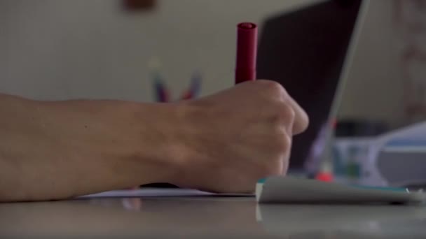 Vue latérale rapprochée de la table dans le bureau avec ordinateur portable et papeterie et un dessin à la main avec marqueur rouge. Homme dessin à la main avec marqueur rouge et prise sellotape . — Video