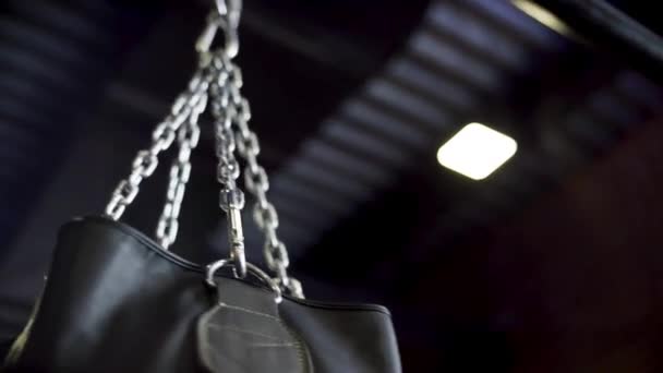 Close-up view of silver chain and swaying black punching bag, action, sport concept. Swinging chain with hanging boxing pear on black ceiling background. — Stock Video