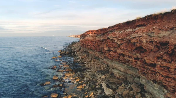 Rocky reef Shore. Skott. Ovanifrån kuststräcka av steniga havsstrand klippor rött med hål och sticker stenar. Vackra blå havet kommer och går i vågor — Stockfoto