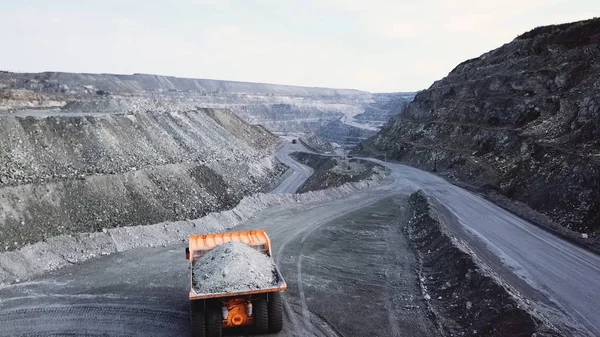 La camioneta está en la cantera. Vista superior de la conducción de camión volquete naranja con escombros en la carretera a cielo abierto. Transporte pesado en la industria minera — Foto de Stock