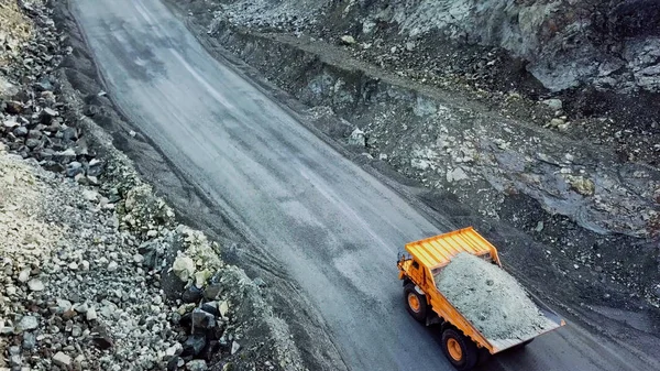 Dump truck is at quarry. Top view of driving orange dump truck with rubble on road open pit. Heavy transport in mining industry