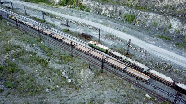Diesel locomotive is pushing dump-car filled with rubble stone in the background of a quarry for limestone mining