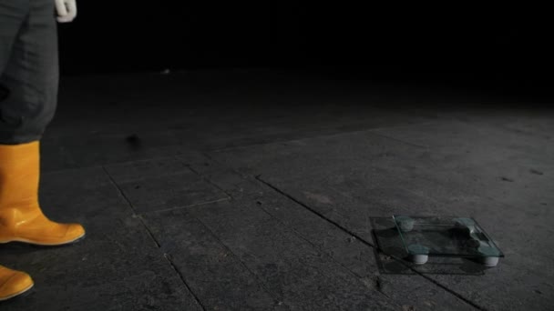 Close-up of man standing on scales. Close-up of workers feet in jeans and rubber boots stand on scales lying on gray concrete in dark room — Stock Video