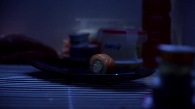 Suşi roll plaka üzerinde Close-up. Yalnız suşi roll somon ve peynir ile el Siyah eldiven alır siyah plaka üzerinde olduğunu