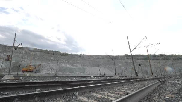 Ferrocarril sobre fondo de hoyo abierto. Ferrocarril pasando por la industria minera con excavadora de pie en segundo plano — Vídeo de stock