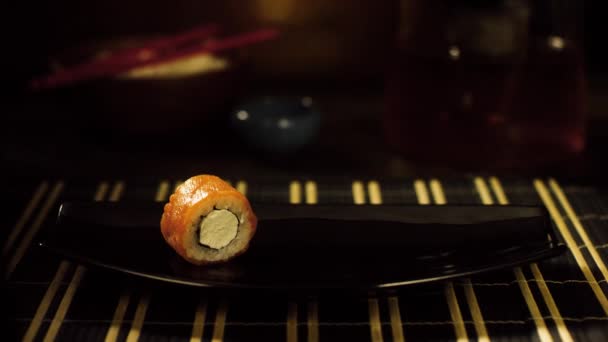 Gros plan du rouleau de sushi sur l'assiette. Rouleau de sushi solitaire avec saumon et fromage est sur plaque noire, qui prend main dans le gant noir — Video