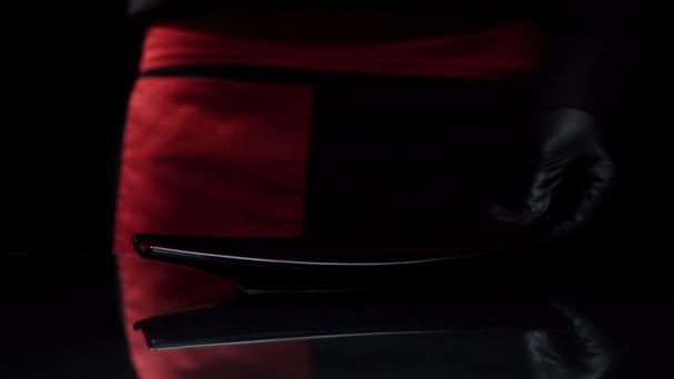 Sushi chef met rouleau de sushi sur l'assiette. Gros plan chef en tablier noir mains dans des gants met un rouleau de sushi sur l'assiette et l'emporte .