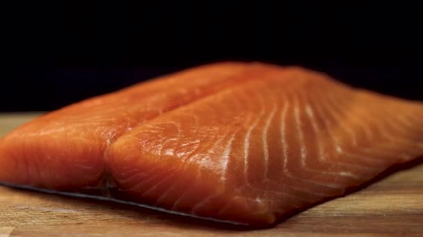 Close-up of juicy piece of salmon. Juicy fresh and red slice of salmon meat lying on wooden board on black background — Stock Video