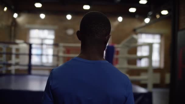 Man stands in boxing gym. Back view of young African American waiting for when to start boxing training