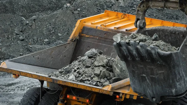 La excavadora llena el camión volquete. Cubo excavadora primer plano carga piedras en el cuerpo de camión volquete en la minería o la construcción de algo — Foto de Stock