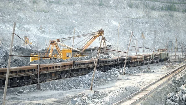 Excavator and railway with ore. Excavator fills with ore rail cars in background of open pit. Heavy transport in mining industry