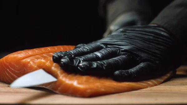 Chef de cerca con trozo de salmón rojo. El chef profesional en guantes negros sostiene un trozo de salmón fresco y está listo para cortarlo — Foto de Stock
