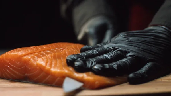 Chef de cerca con trozo de salmón rojo. El chef profesional en guantes negros sostiene un trozo de salmón fresco y está listo para cortarlo — Foto de Stock