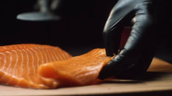 Chef de cerca con trozo de salmón rojo. El chef profesional en guantes negros sostiene un trozo de salmón fresco y está listo para cortarlo — Foto de Stock