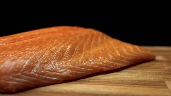 Primer plano del jugoso trozo de salmón. Jugosa rebanada fresca y roja de carne de salmón acostada sobre tabla de madera sobre fondo negro — Foto de Stock