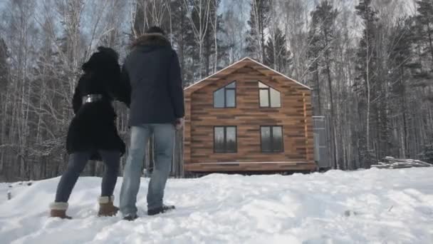 Boldog fiatal pár faház közelében. Stock. Pár áll a ház az erdő közelében, a téli — Stock videók