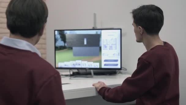 Två män utvecklar utformningen av huset bakom en dator. Lager. Mannen bakom en laptop utveckla en modell av huset. Design av 3d-modeller — Stockvideo