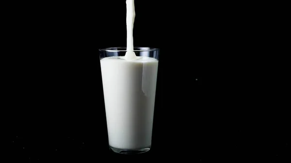 Primer plano en vaso vierta yogur blanco. Una trampa. En vidrio grande transparente vierta líquido grueso blanco sobre fondo negro aislado — Foto de Stock