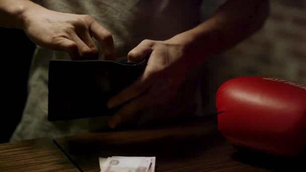 Close up of man hands holding a open leather wallet with a few coins inside over a old wooden table with paper money lying on it. Masculino colocando moedas em notas no quarto escuro, rublos russos . — Vídeo de Stock