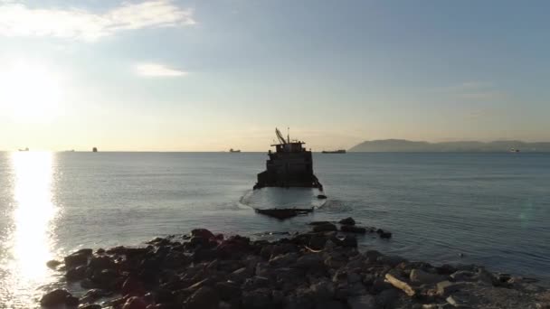 Vor blauem, bewölktem Himmel und strahlendem Sonnenhintergrund versank das rostige Schiffswrack in einem blauen Meer. Schuss. Boot in Küstennähe abgestürzt und im Wasser reflektiertes Sonnenlicht. — Stockvideo