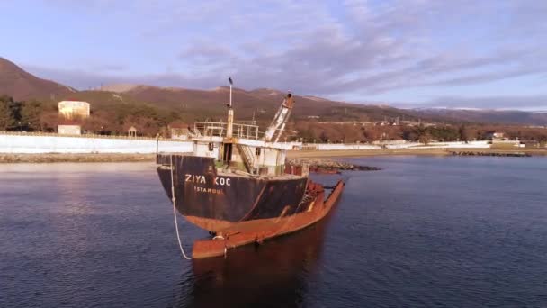 Gammal övergiven båt på stranden vid havet med en kustlinje och berg på bakgrunden. Skott. Förlist, sjönk fartyget på steniga stranden mot blå, molnig himmel. — Stockvideo