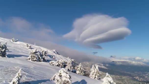 Schöne Luftaufnahme von schneebedeckten Berghängen und Bäumen auf blauem Himmel Hintergrund. Schuss. Ungewöhnliche massive Wolke am strahlenden Himmel über schneebedeckten Felsen und Kiefern. — Stockvideo