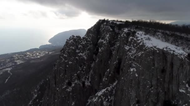 Der Hang des hohen Felsmassivs ist mit Kiefern bedeckt und von Nebelschwaden bedeckt. Schuss. Antenne für den bewaldeten Berghang in schweren, grauen Wolken und Küste mit kleiner Stadt. — Stockvideo