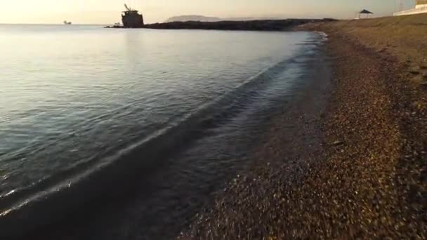 靠近海岸线与砾石和海浪在海滩上的日落天空背景。拍摄。石质海岸上的小浪, 背景上有几艘船. — 图库视频影像