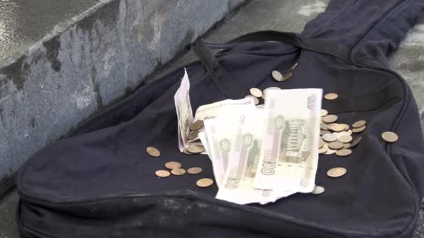 Geld fällt auf schwarzen Gitarrenkoffer auf dem Bürgersteig der Stadt. Nahaufnahme für Papiergeld und Münzen auf schwarzem, leerem Gitarrenetui liegend, Armutskonzept. — Stockvideo