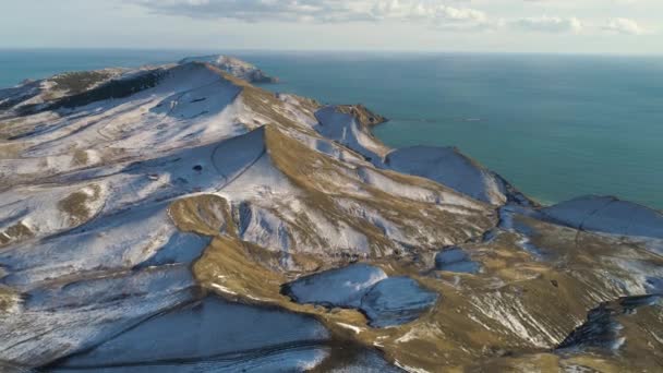 Luftaufnahme von schneebedeckten Felsen, blauem Meer, auf bewölktem Himmel Hintergrund. Schuss. Schneebedeckte Hügel in Island am Meer an einem Wintertag. — Stockvideo