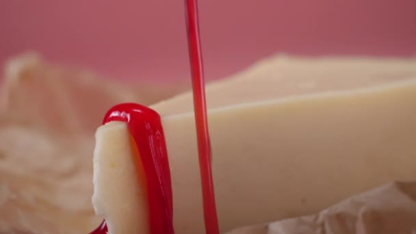 Close-up de deliciosa fatia de cheesecake derramado por fina corrente de geléia de morango. Moldura. Isolado em rosa — Vídeo de Stock