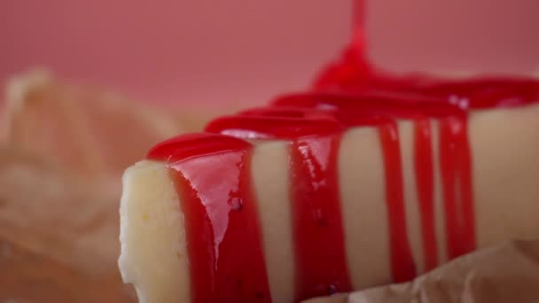 Γκρο πλαν, νόστιμη φέτα cheesecake που χύνεται από λεπτή ροή του μαρμελάδα φράουλα. Πλαίσιο. Απομονωμένα σε ροζ — Αρχείο Βίντεο