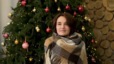 Noel ağacı yanında battaniye dinlenme ile iç çamaşırı rahat genç kadın. Beyaz bir kazak ve sıcak çorap gülümseyen kız güzel bir şekilde dekore edilmiş bir Noel ağacına sıcak bir battaniye sarılmış oturur