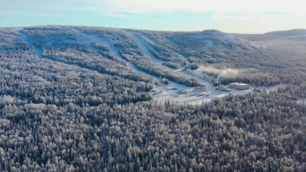 Vista superior de la base de esquí con pistas en la montaña. Filmación. Panorama de montañas cubiertas de nieve con pistas de esquí y recreación entre bosques de coníferas en día claro de invierno — Vídeos de Stock