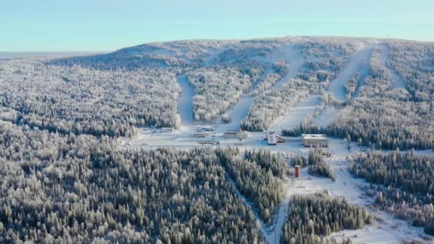 Widok z góry ośrodka narciarskiego u podnóża góry. Materiał filmowy. Ośrodek narciarski zaciszne, u stóp wzgórza ze stoków narciarskich jest popularne w sezonie zimowym. Jasny słoneczny dzień na stoki narciarskie ośrodka sportów zimowych — Wideo stockowe