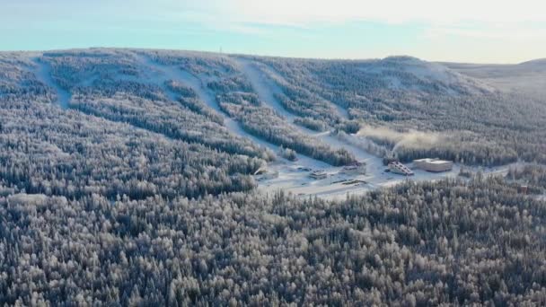 Blick von oben auf das Skigebiet am Fuße des Berges. Filmmaterial. Abgelegenes Skigebiet am Fuße des Hügels mit Skipisten ist in der Wintersaison beliebt. Klarer sonniger Tag auf den Skipisten des Wintersportortes — Stockvideo