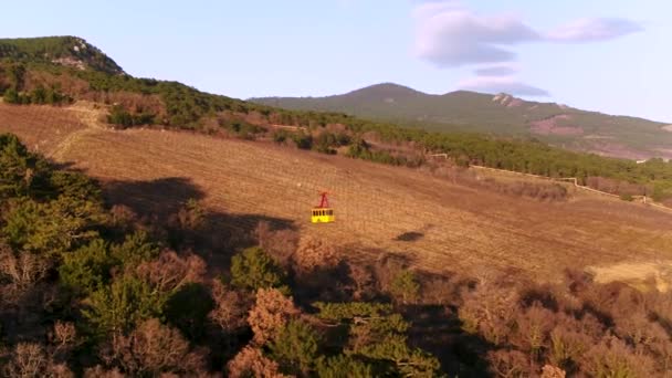 Antenne voor geel kabelspoorweg met bewegende op de achtergrond van de helling bomen. Schot. Kabelbaan over beboste heuvel helling in zonsondergang beweegt. — Stockvideo