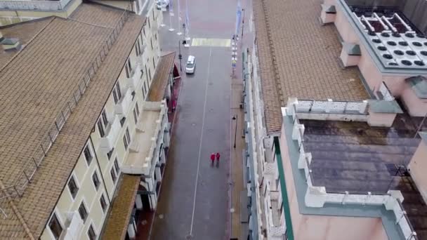 Vista superior de dos personas caminando bajo la lluvia. Dos personas van a impermeables rojos en la lluvia en la calle húmeda del casco antiguo — Vídeo de stock