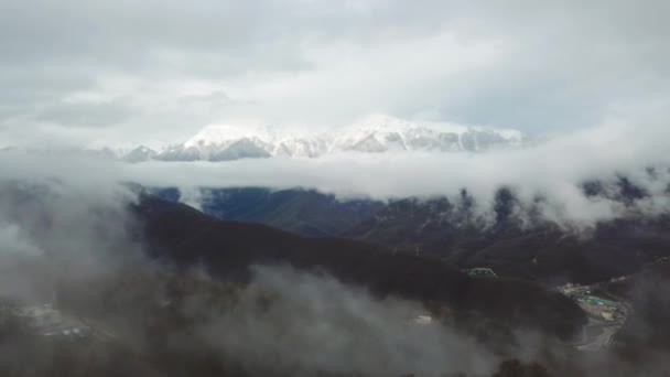 Bovenaanzicht door wolken op de besneeuwde toppen van de vallei. Prachtige landschap van bergtoppen maken haar weg door lage wolken die afdalen in de kloven van bergdal — Stockvideo