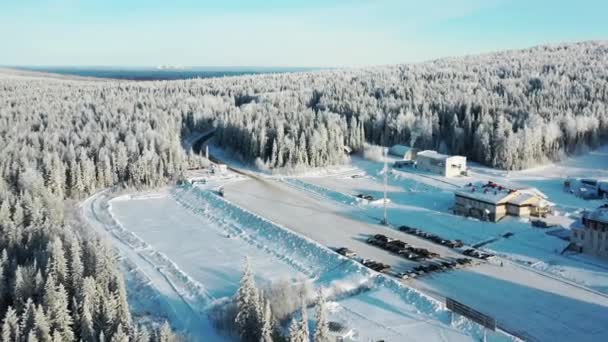 近代的なスキー基地、ホテル、青い空を背景に冬の森に囲まれた駐車場の空撮。映像。上からの眺め — ストック動画
